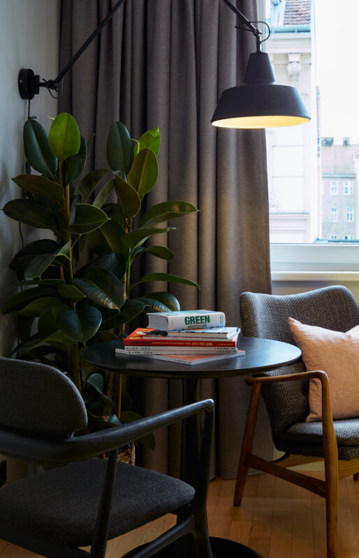 Cozy interior scene featuring a small round table with books, two stylish chairs, a potted plant, and a lamp.
