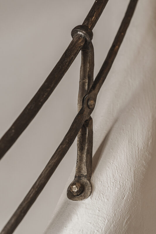 Close-up of a decorative metal bracket connecting curved rods on a white wall in Stieg'nhaus interior.