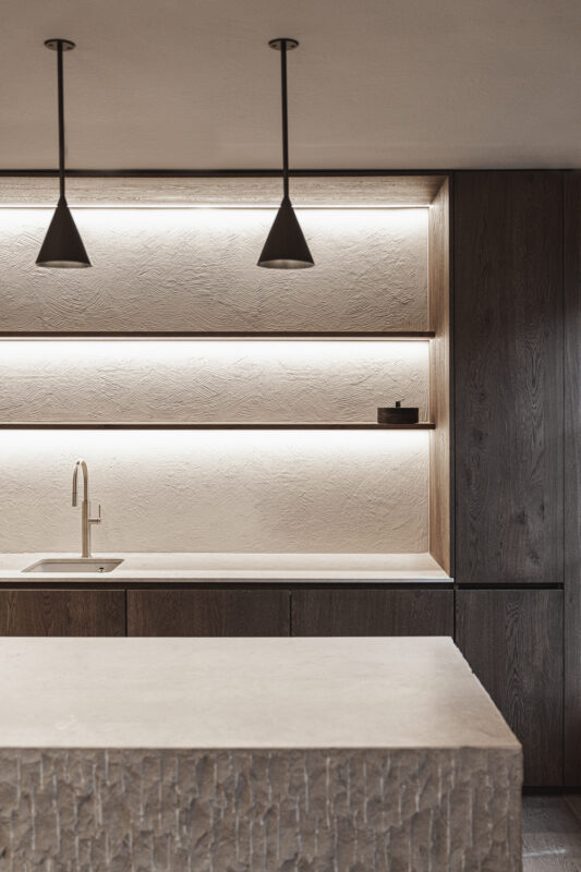 Modern kitchen interior featuring a stone countertop, wooden cabinetry, and minimalist pendant lighting.