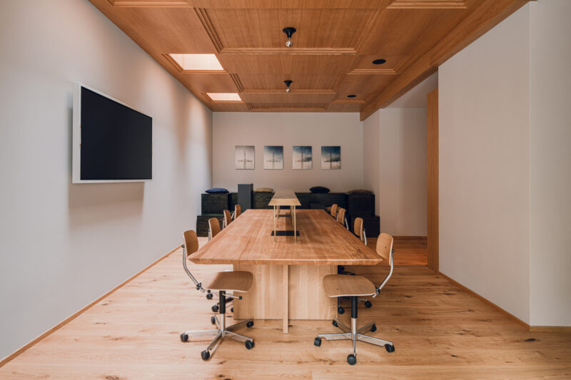 Modern conference room with a wooden table, chairs, and a large screen, featuring artwork on the walls.