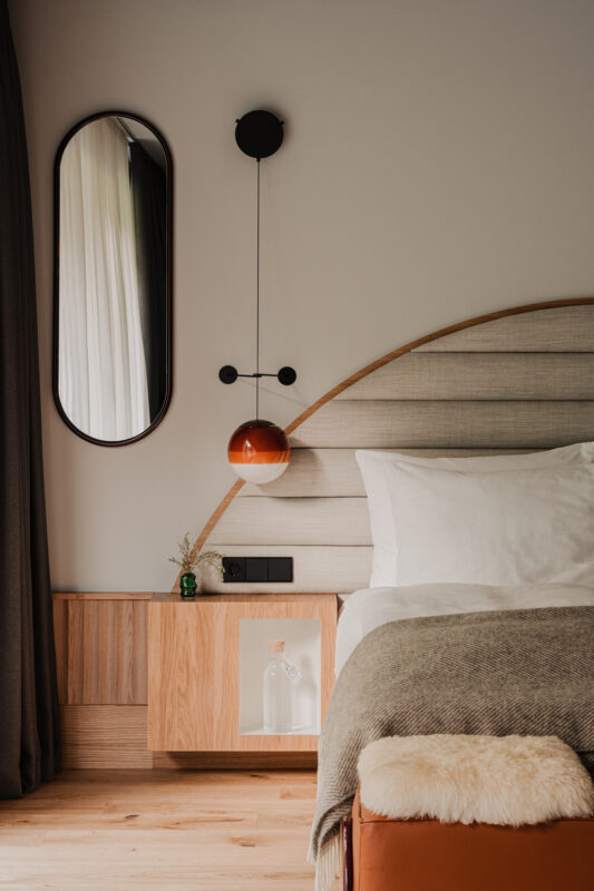 Modern bedroom featuring a curved headboard, a round mirror, and a pendant light above a nightstand.