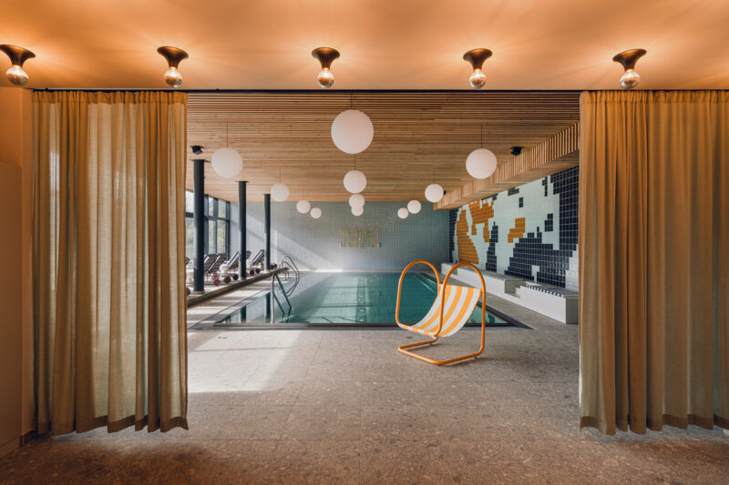 Indoor swimming pool area with a modern design, featuring a pool, orange lounge chair, and decorative lighting.
