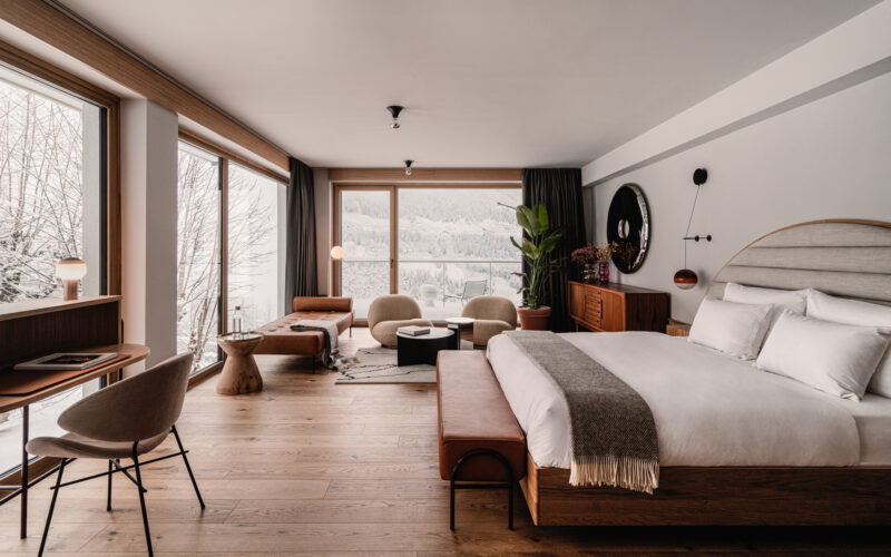 Modern hotel room featuring a large bed, seating area, and panoramic windows showcasing a snowy landscape.