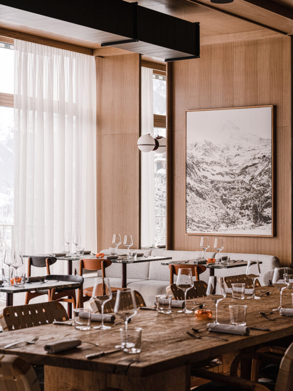 Modern restaurant interior featuring wooden tables, elegant glassware, and a large mountain landscape artwork.