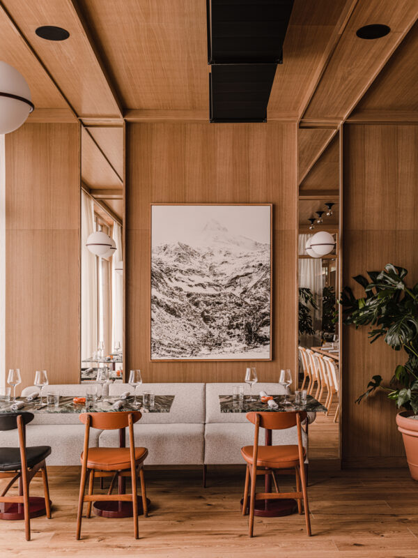 Modern restaurant interior featuring wooden walls, a large mountain photograph, and a cozy dining area with chairs and tab...