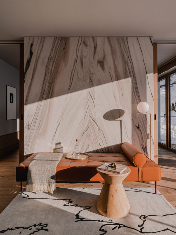 Modern living room featuring a brown leather sofa, a wooden side table, and a marble wall with natural patterns, illuminat...