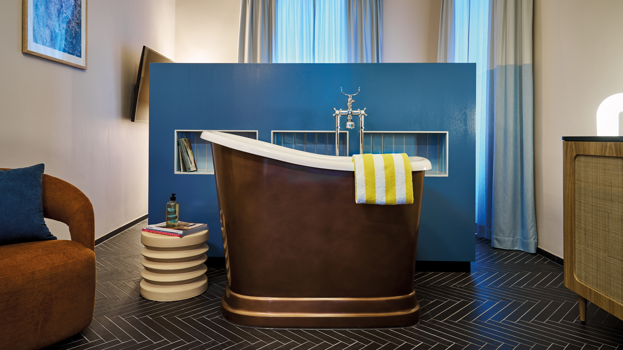 Freestanding copper bathtub with a striped towel, set in a stylish room featuring blue accents and modern decor.