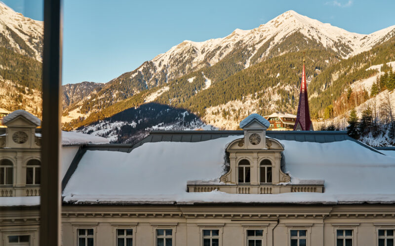 View from a window in a junior suite at Badeschloss, showcasing snow-covered mountains and a church spire.