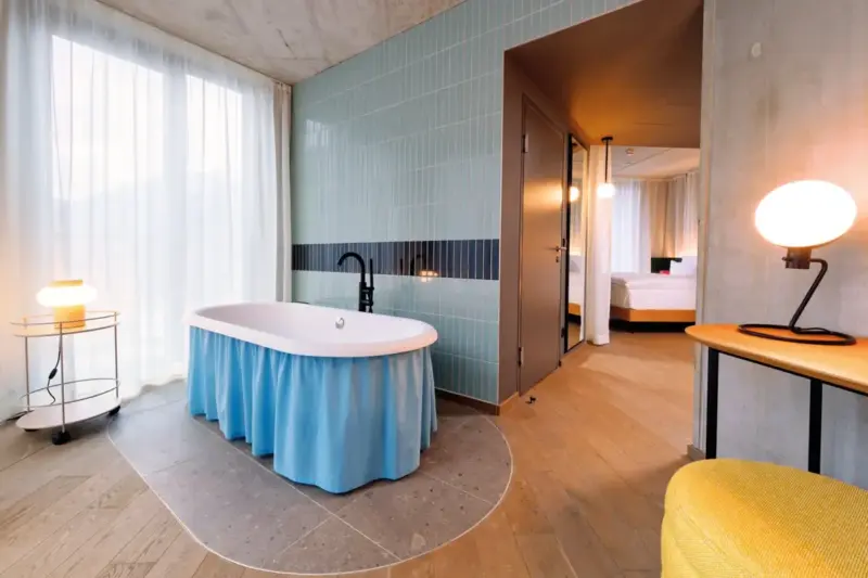 Interior view of a junior suite featuring a freestanding bathtub with a blue skirt, large windows, and modern decor.