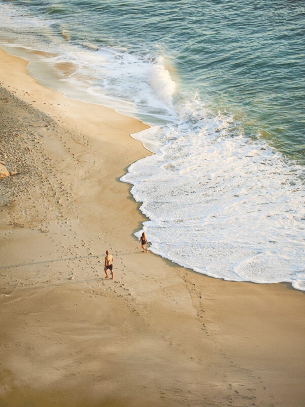 Two people walking along a sandy beach with gentle waves lapping at the shore in South Africa.