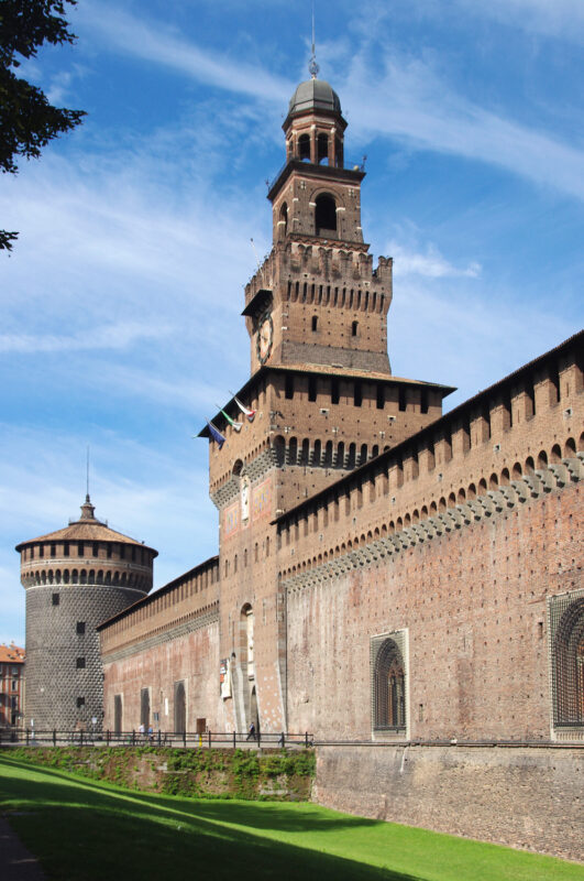 Sforza Castle in Milan, featuring a tall tower and fortified walls under a blue sky.
