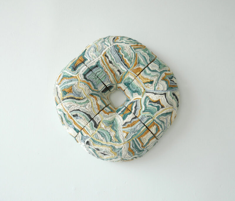 Coloured porcelain wall sculpture titled "Blue and Green Wall Ribbon," featuring swirling patterns in blue, green, and white.