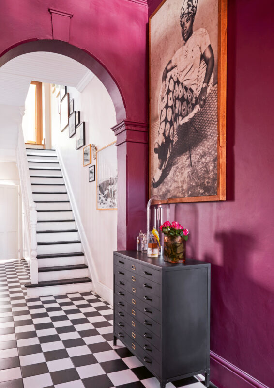 Vibrant hallway with a purple wall, black and white checkered floor, and a large portrait of a woman.