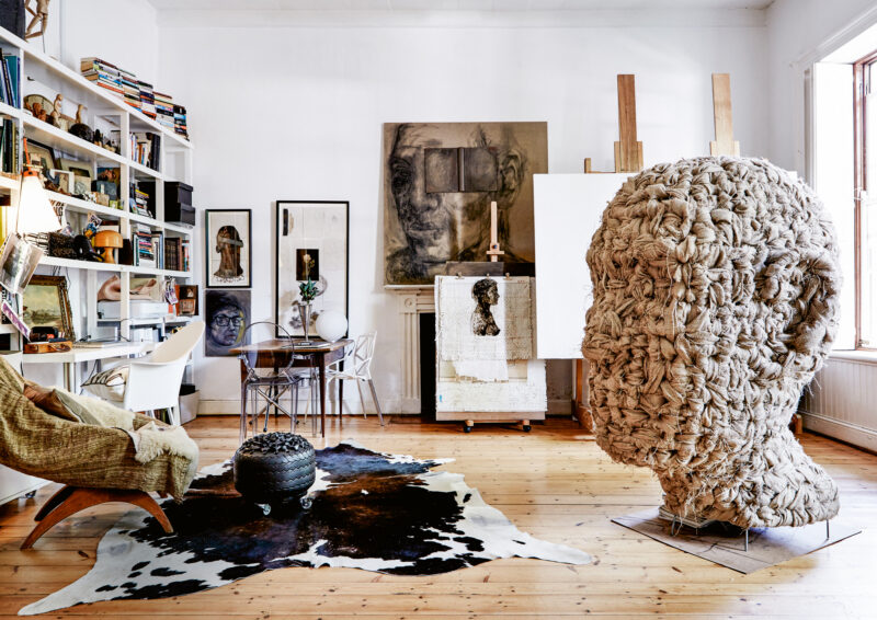 Artistic interior featuring a large woven head sculpture, bookshelves, and a cozy seating area with a cowhide rug.