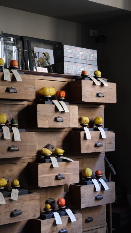 Wooden drawers filled with various gourds and pumpkins, each labeled with tags, against a dimly lit background.