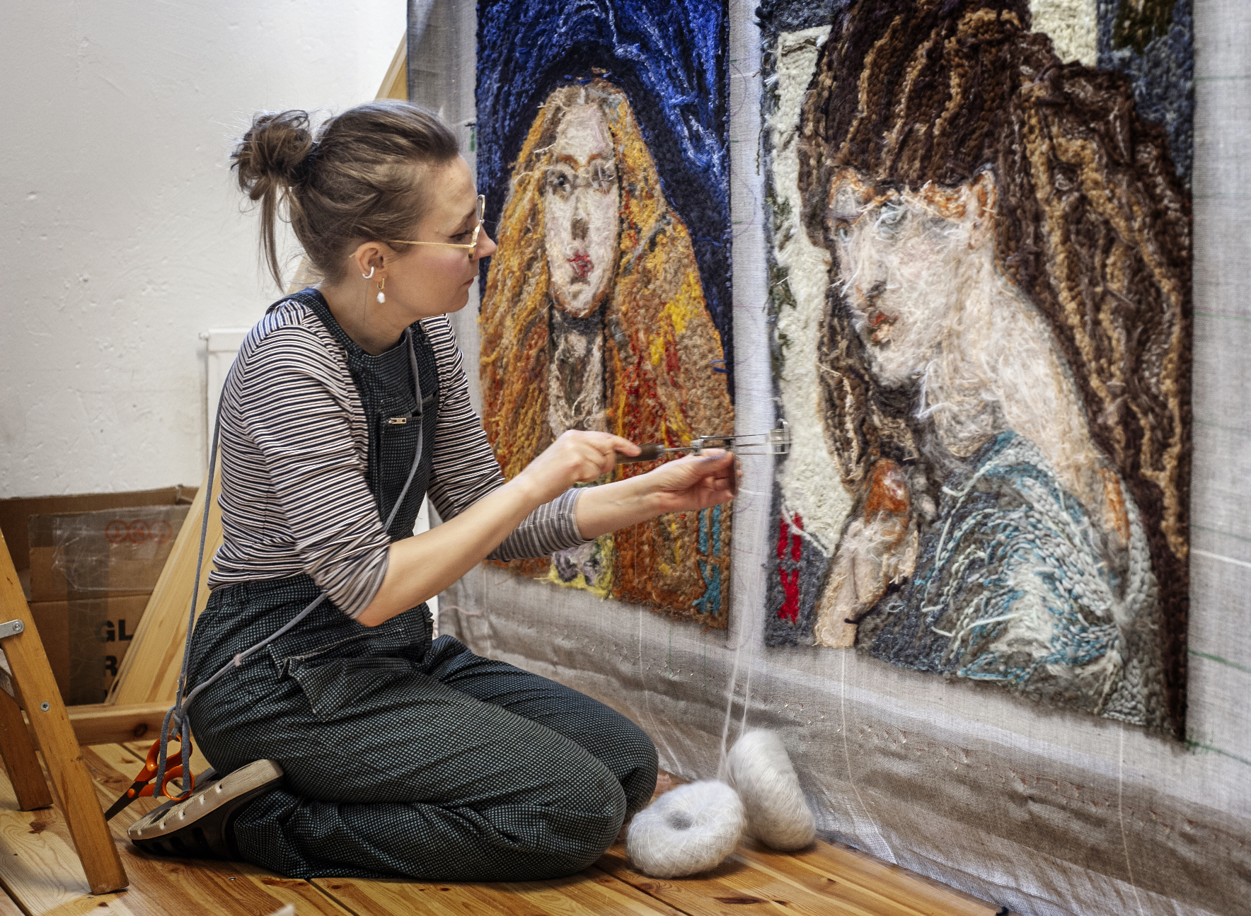 Artist Hanna-Kaisa Korolainen working on a textured textile artwork featuring two female portraits.