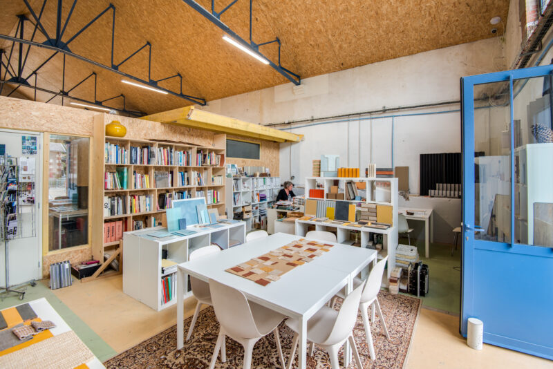 Bright workspace with bookshelves, a large table, and a person working, showcasing a creative environment at ICI Nantes.