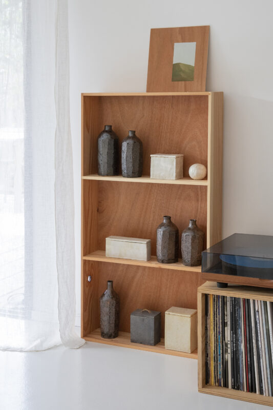 Wooden shelving unit displaying various decorative objects, including bottles and boxes, beside a record player.