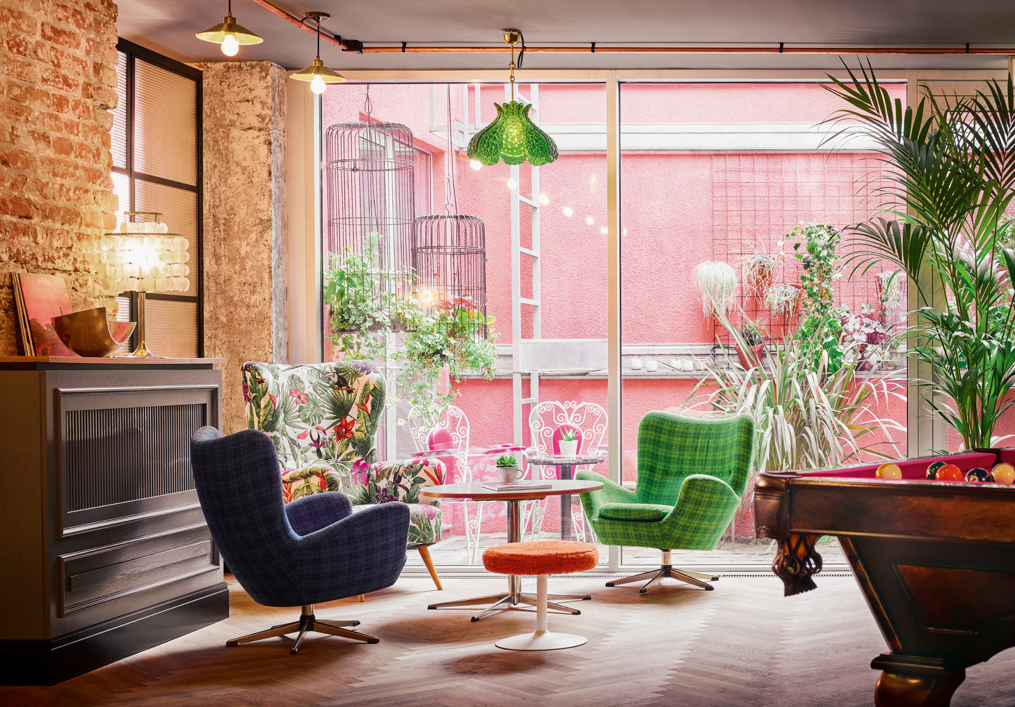 Colorful lounge area featuring patterned chairs, a round table, and greenery visible through large windows.