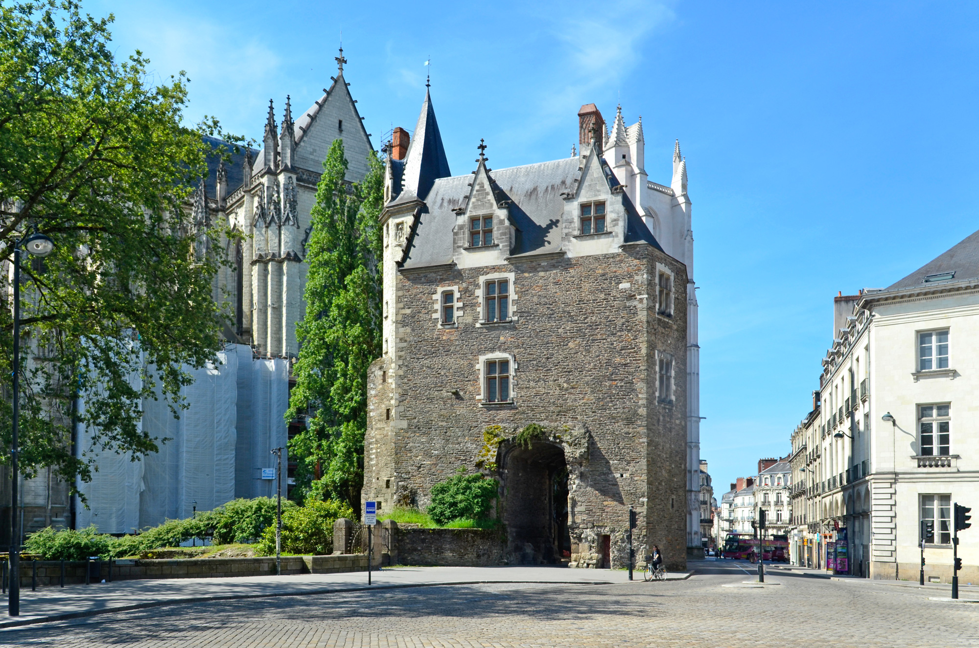 Historic stone building with a tower, surrounded by greenery, near the Porte Saint-Pierre in Nantes.
