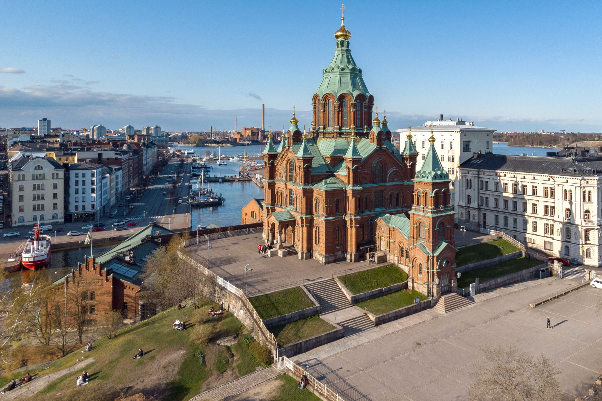 Uspenski Cathedral in Helsinki, Finland, with a clear sky, surrounded by city buildings and a harbor.