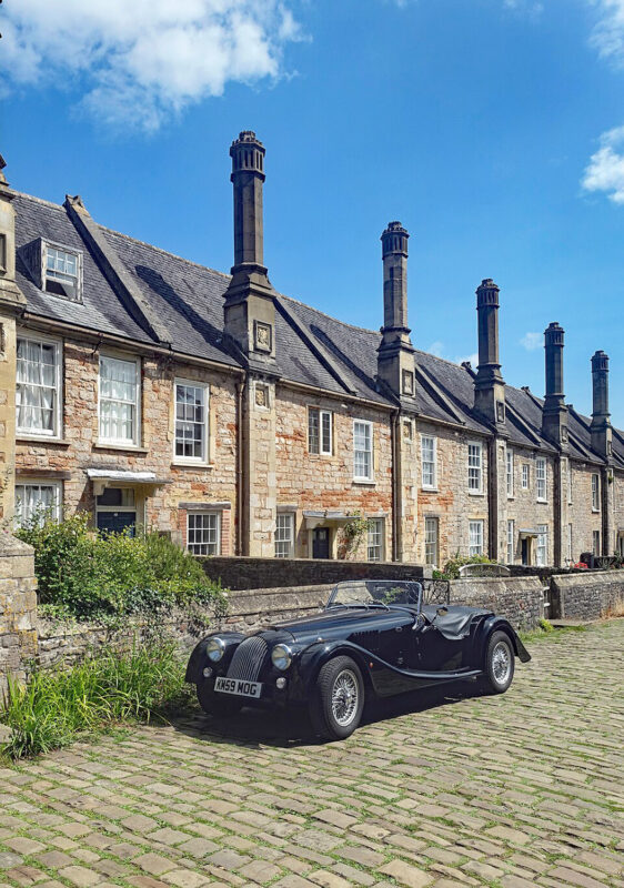 Black open-top car parked in front of historic stone houses with tall chimneys in Vicars Close.