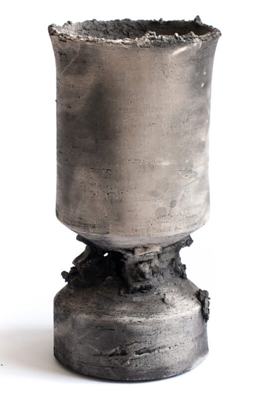 Ceramic sculpture with a textured, gray surface, featuring a cylindrical top and a wider base, showcasing an artistic design.