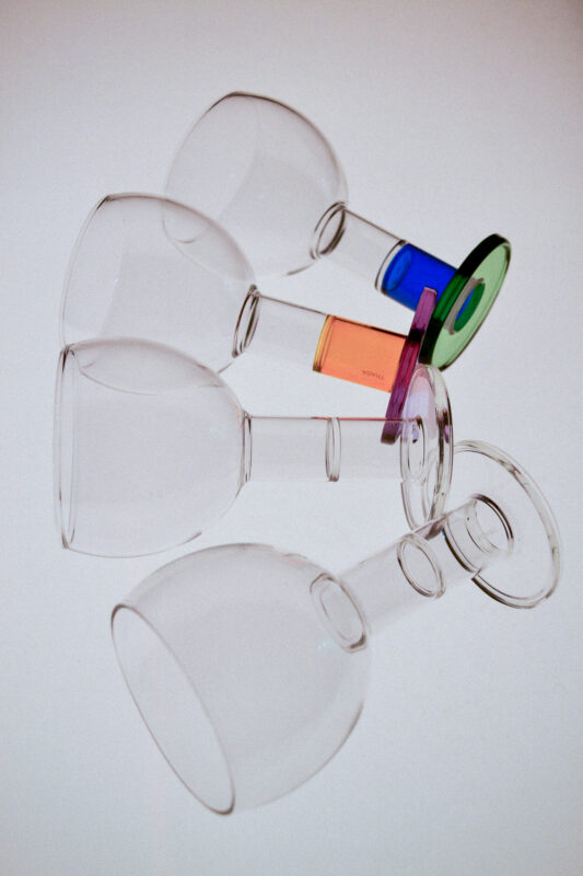 Four transparent wine glasses arranged at an angle, each with colorful circular coasters in vibrant hues.
