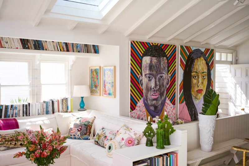 Bright living room featuring two large colorful portraits, a white sofa with decorative pillows, and a bookshelf.