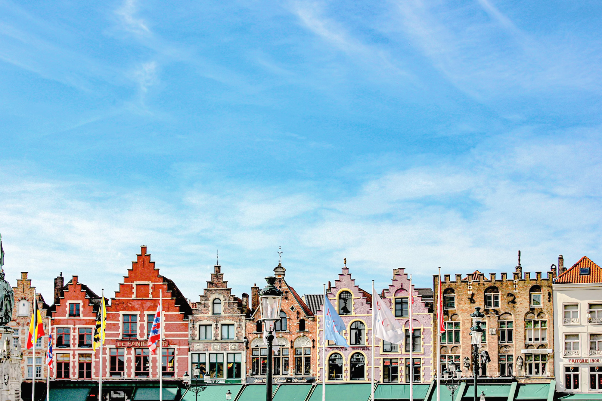Historic buildings with colorful facades and flags along a waterfront under a blue sky.