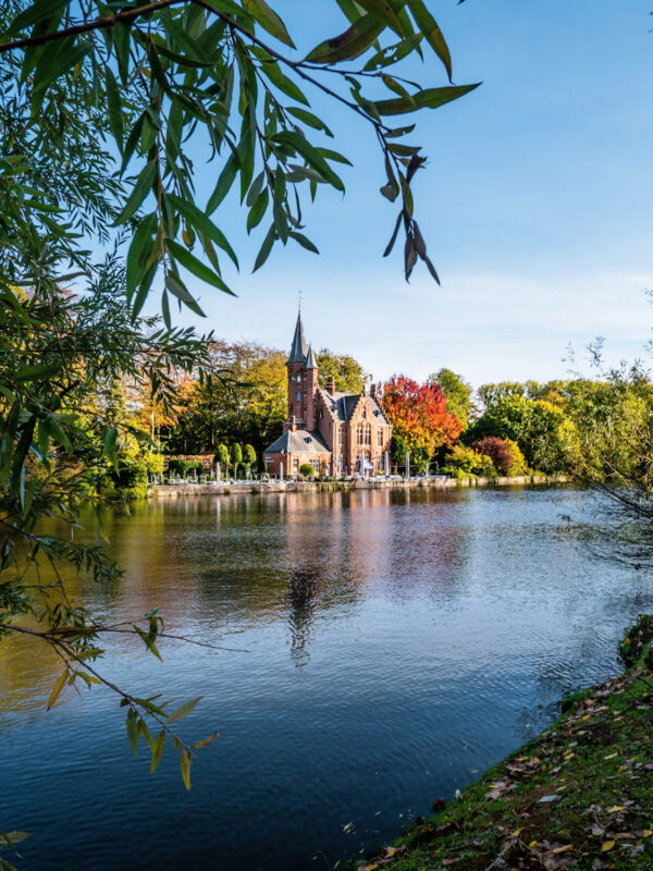 Scenic view of a church by a calm lake, surrounded by autumn foliage and clear blue skies.