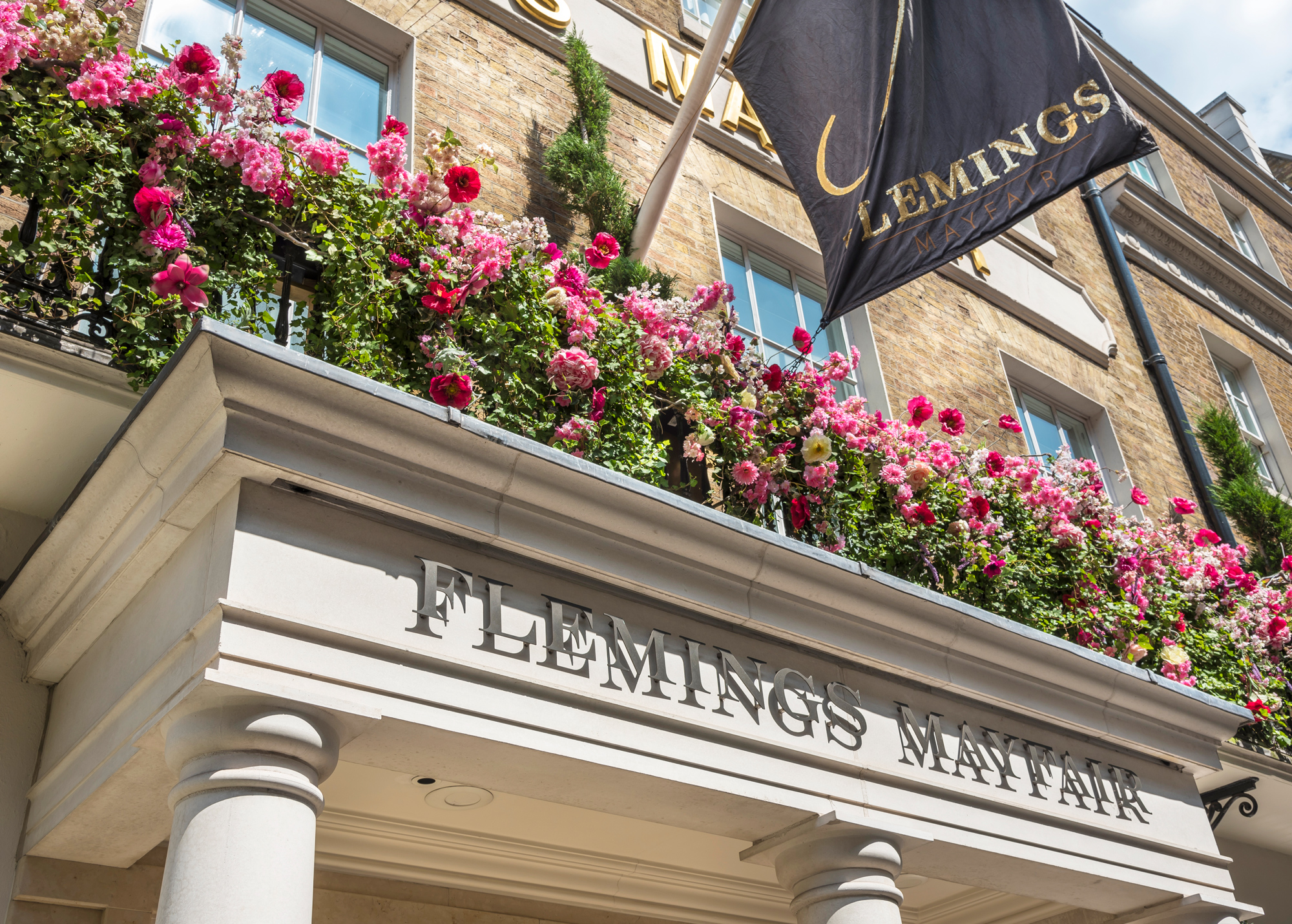 Floral display above the entrance of Flemings Mayfair, featuring the hotel's name and a flag.