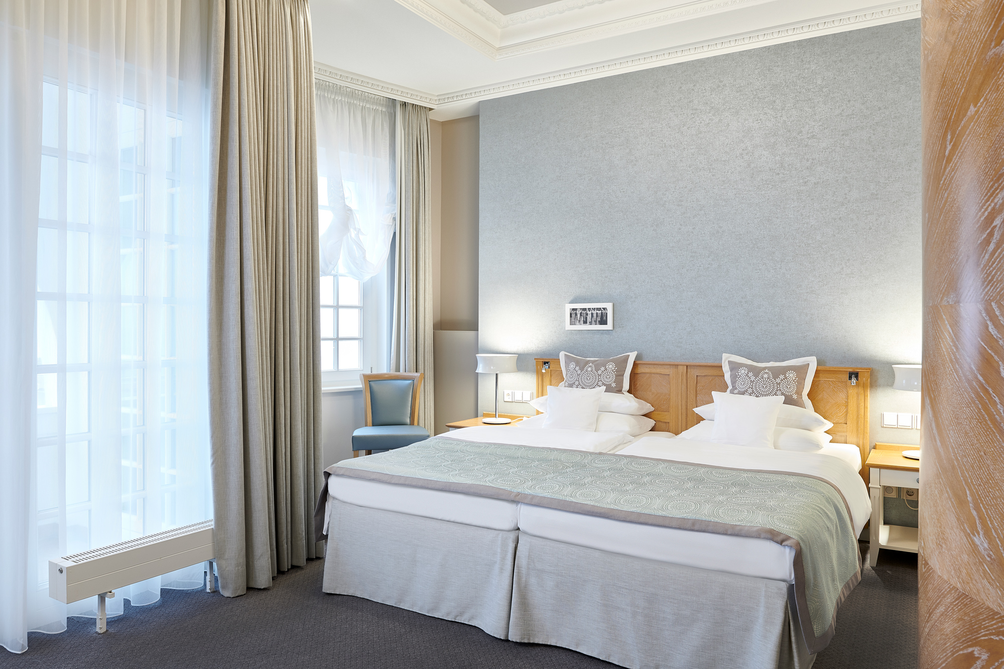 Junior suite bedroom at Kurhaus Binz, featuring a double bed, elegant decor, and large windows with sheer curtains.