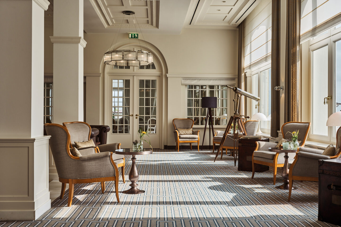 Bright, elegant lounge area with armchairs, a telescope, and large windows, featuring a patterned carpet and soft lighting.