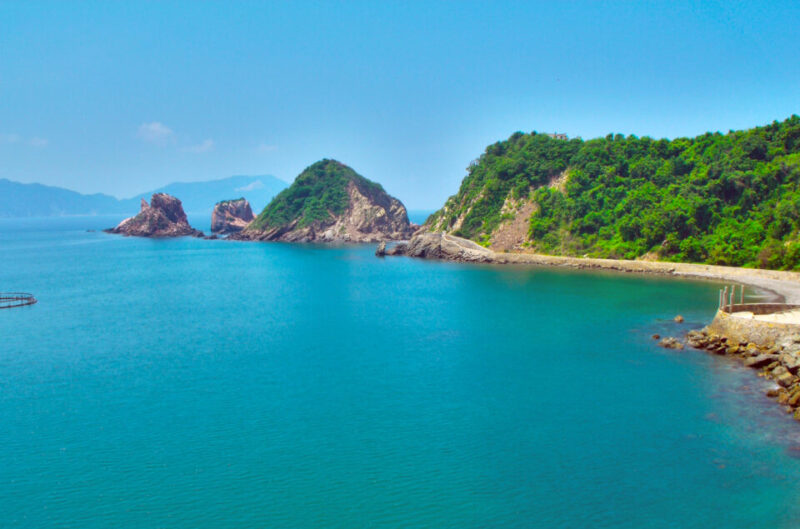 Scenic view of Bahia de Melaque with rocky formations and lush greenery along the coastline under a clear blue sky.