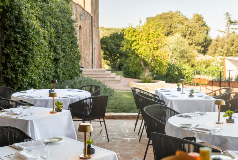 Outdoor dining area at Borgo Dei Conti Resort, featuring tables set with white tablecloths and greenery in the background.