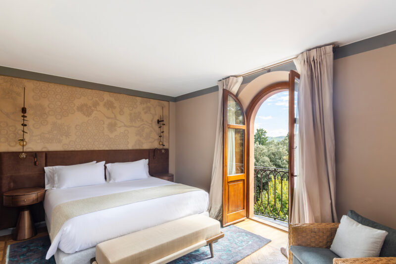 Elegant bedroom in Borgo Dei Conti Resort with a large window, showcasing a view of greenery and natural light.