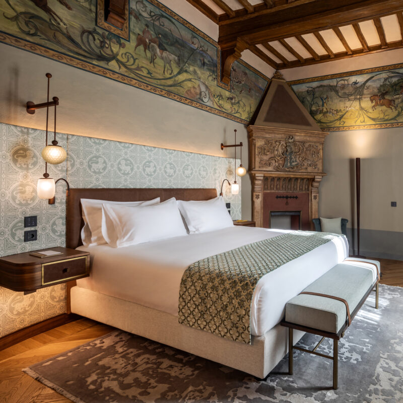 Elegant suite at Borgo dei Conti Resort featuring a king bed, decorative wall murals, and a vintage fireplace.