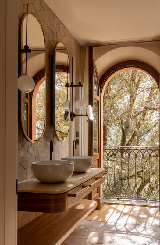 Elegant bathroom in the Borgo Dei Conti Resort's sunset suite, featuring two bowls, mirrors, and a view of trees through a...