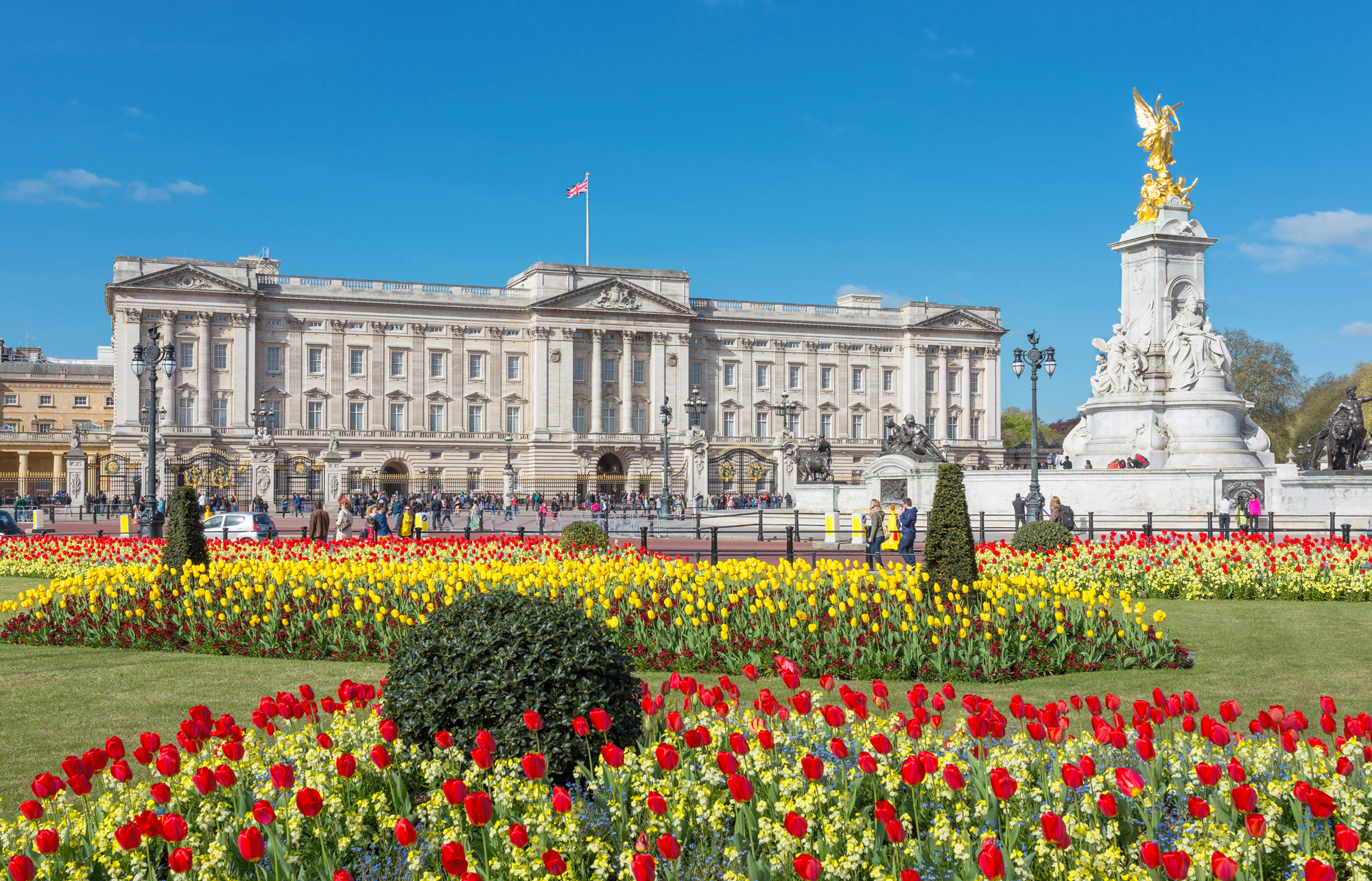Buckingham Palace viewed from the gardens, surrounded by vibrant flower beds in spring.