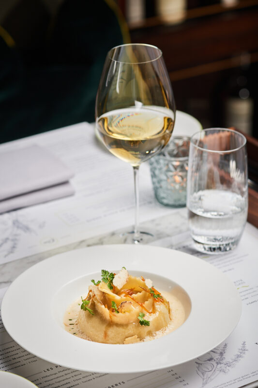 Canneloni served on a white plate, garnished with herbs, alongside a glass of white wine and a water glass.