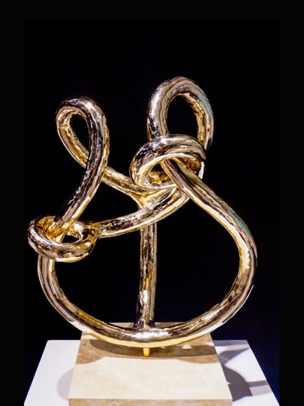 Sculpture of intertwined golden loops on a pedestal against a black background.