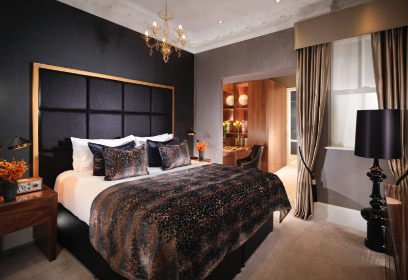 Luxurious bedroom at Flemings Mayfair, featuring a king-size bed with leopard print throw, elegant decor, and warm lighting.