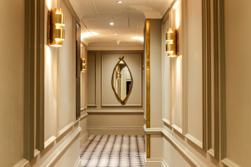 Elegant corridor in Flemings Mayfair, featuring wall sconces and a decorative mirror, with patterned flooring.