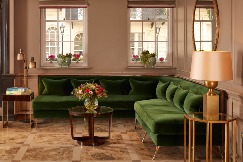 Elegant green velvet sofa in Flemings Mayfair lobby, with a glass coffee table and floral arrangements by the windows.