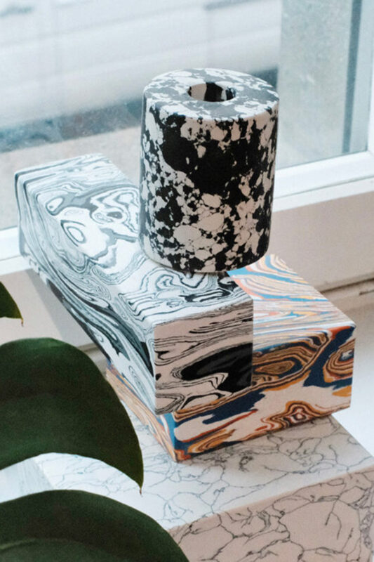 Decorative vases in black and white marble patterns, placed on a colorful, patterned box by a window.