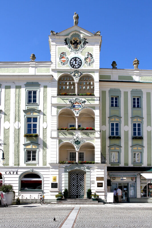 Historic Gmunden town hall with decorative facade, clock, and balconies, set against a clear blue sky.