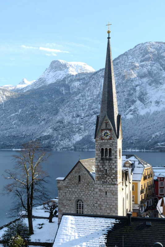 Evangelical church in Hallstatt with a tall spire, surrounded by snow-covered mountains and a lake.