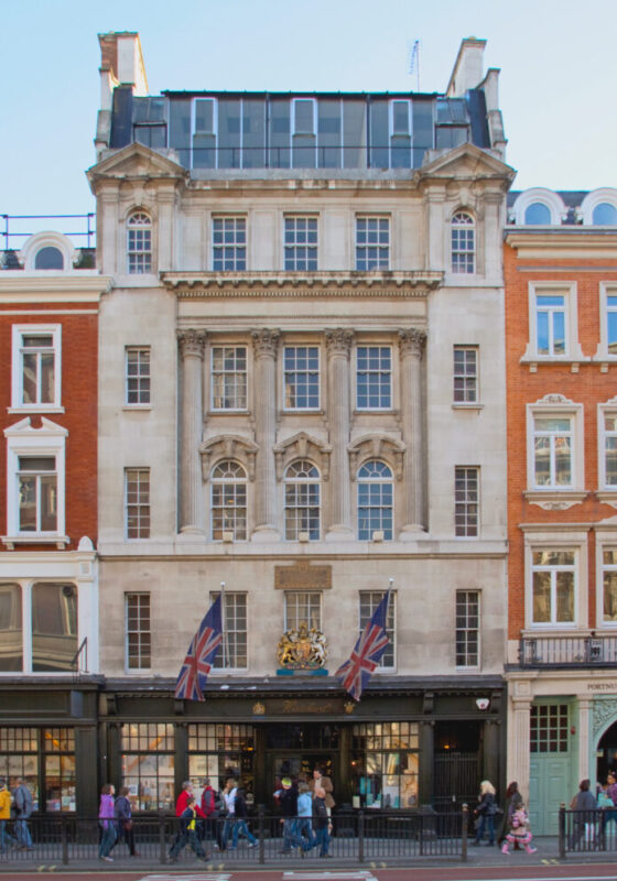 Historic building facade with large windows, British flags, and pedestrians outside, located near Flemings Mayfair Hotel.