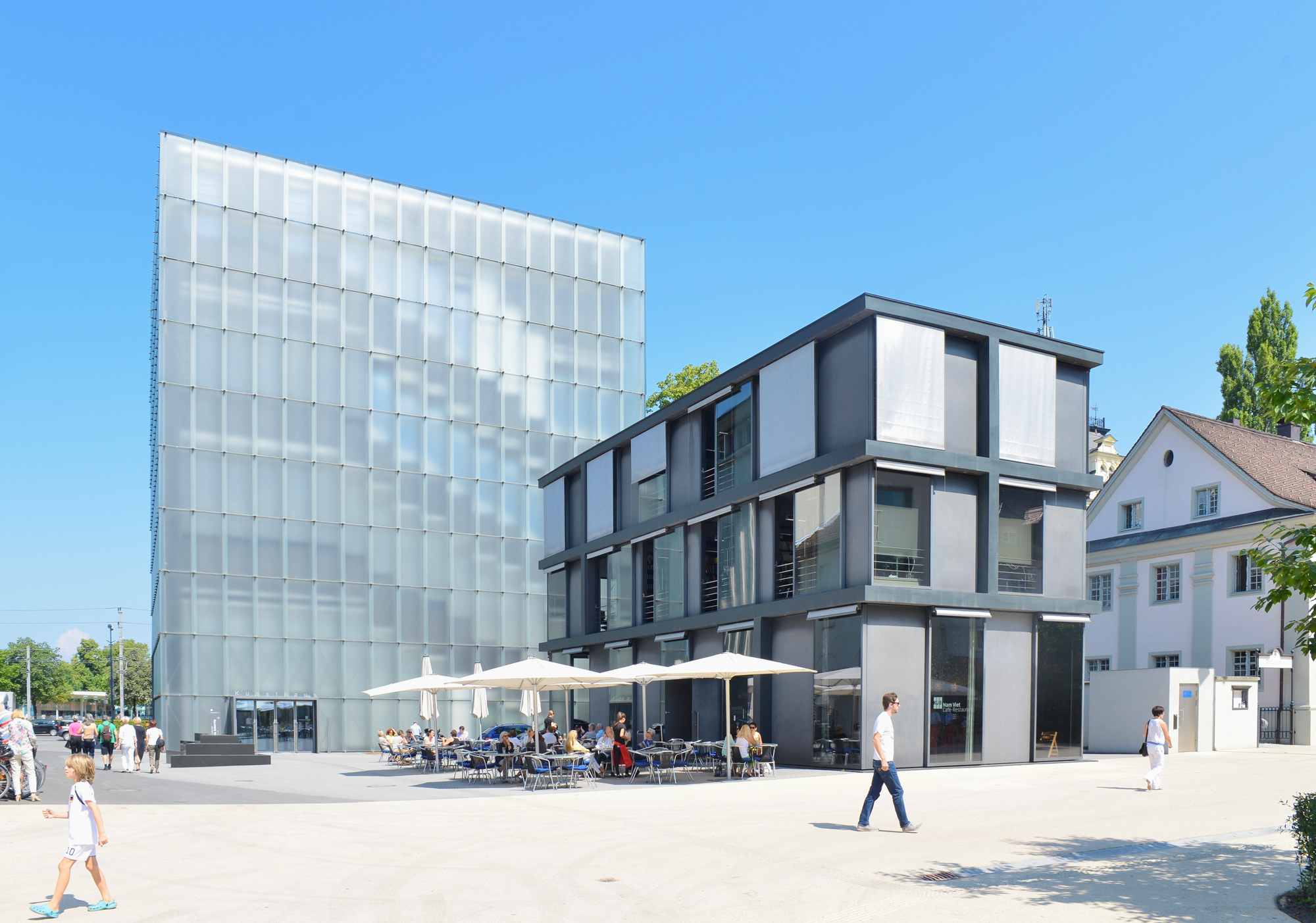 Modern buildings on Kornmarktstraße, featuring a glass structure and a contemporary art house with outdoor seating.